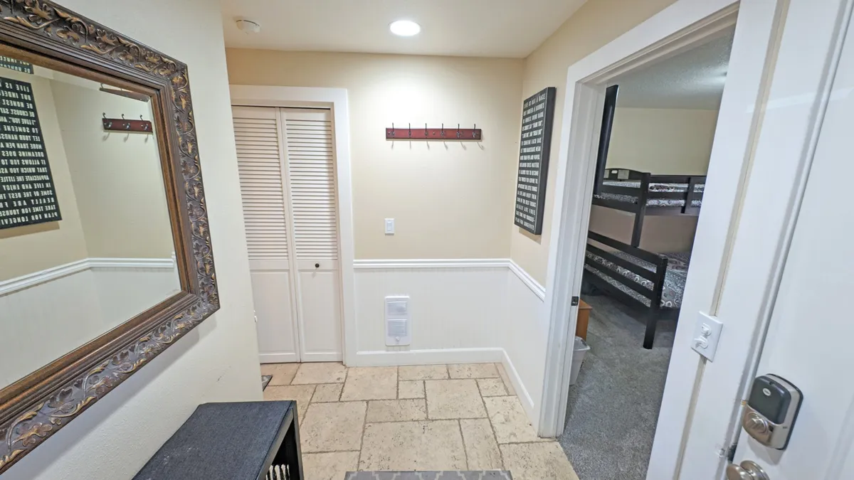 The image shows an inviting entryway with an ornate mirror, wall hooks for coats or bags, and a view into the next room, hinting at the home's layout and flow. The use of warm lighting and practical storage contributes to a welcoming first impression.