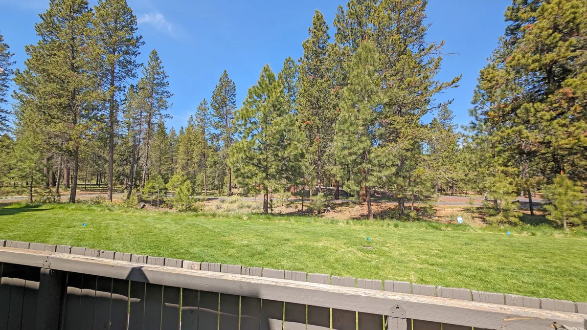 A serene, expansive green lawn set beneath tall pine trees and a clear blue sky. The open area is ideal for outdoor activities like picnicking, nature walks, or watching the sunset, reinforcing the sense of space and natural beauty in the Sunriver area.