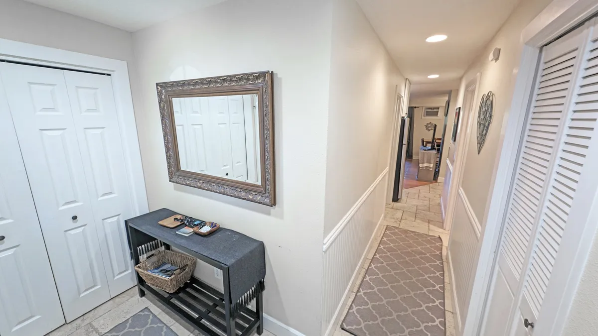 A bright, inviting foyer scene with a mirror, console table, and textured rug. Double doors lead further into the home, suggesting fluid movement between indoor comfort and outdoor escapades. The area is uncluttered and open, evoking a sense of transition and anticipation for new experiences.