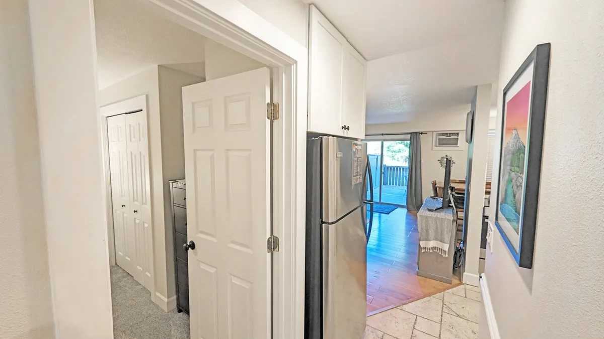 This image highlights a well-lit kitchen area with a refrigerator, doorway leading further into the home, wall artwork, and light flooring. The scene conveys functionality and social potential, hinting at the fully equipped kitchen described in the section.