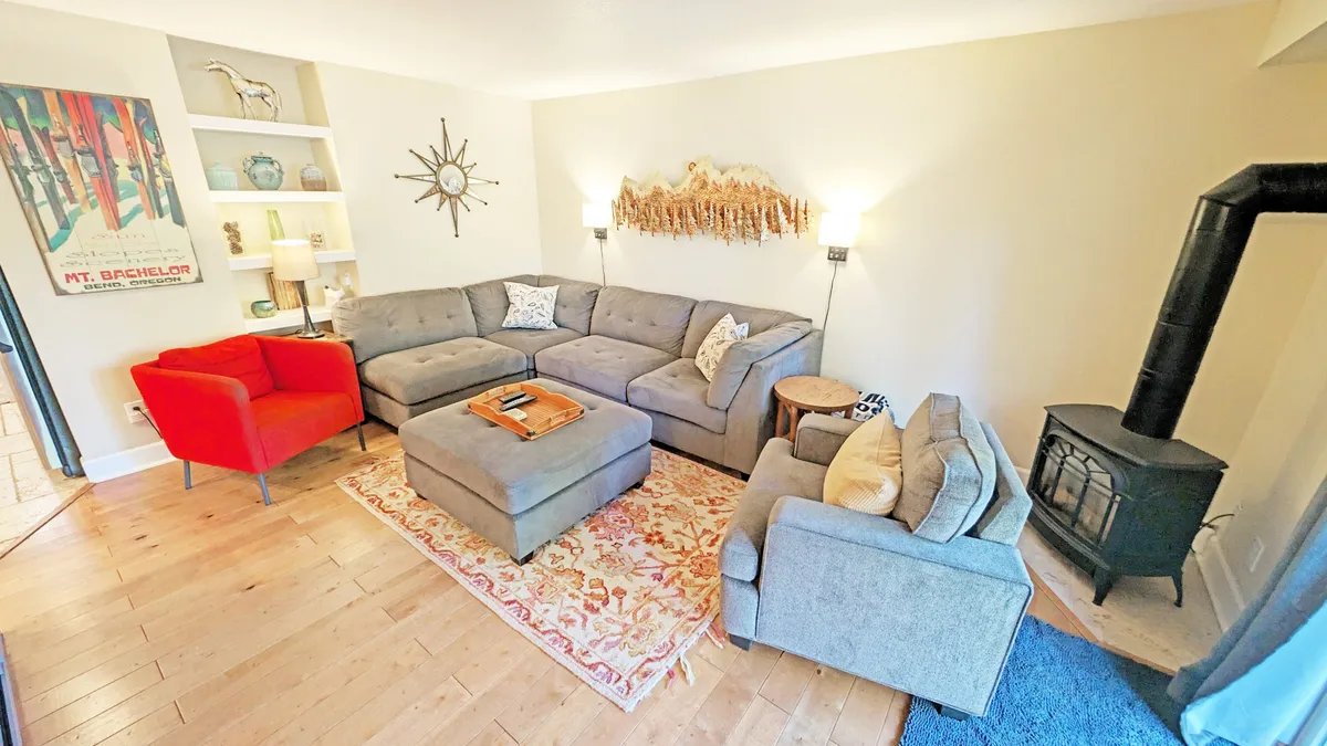 A cozy living area featuring a large sectional sofa and a red accent chair arranged around a wood-burning stove, with decorative wall art adding warmth. The space is designed for relaxation, socializing, and enjoying the fire, perfectly capturing the heart of the open-plan living area.