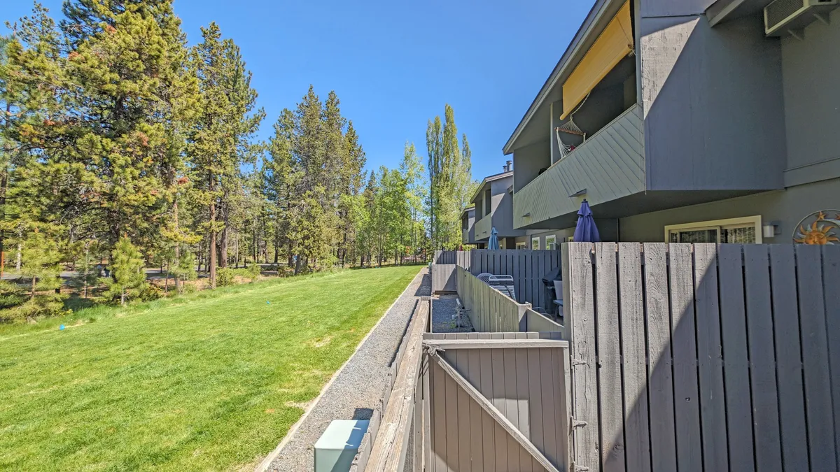 This exterior image displays a lush green lawn bordered by tall trees, with balconies of the building visible in the background. The setting feels peaceful and family-friendly, suggesting an inviting outdoor environment where children can play and families can gather.