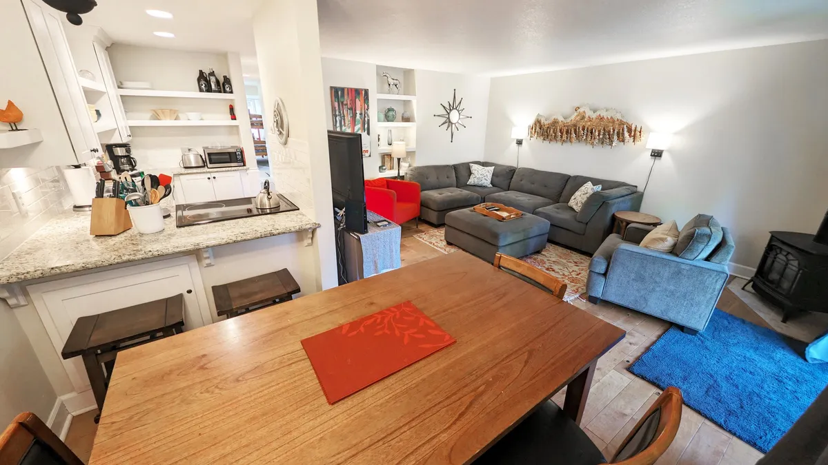 This hero image showcases an inviting interior with a modern dining table set for gatherings, a cozy sofa in the living area, tasteful decorative wall art, and a sleek kitchen counter—all set in an open-concept layout that feels both welcoming and stylish.