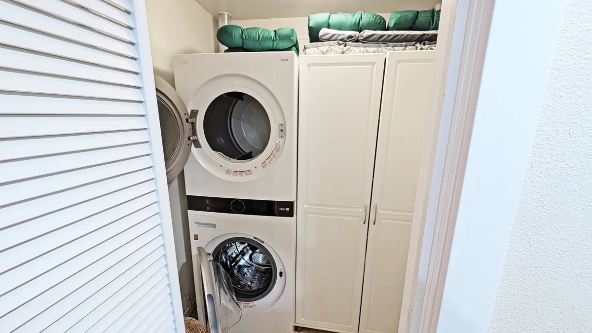 This image showcases a practical laundry area featuring a stacked washer and dryer, white cabinetry for storage, and neatly folded green blankets. The space is well-organized and clean, highlighting the convenience of in-unit laundry for guests.