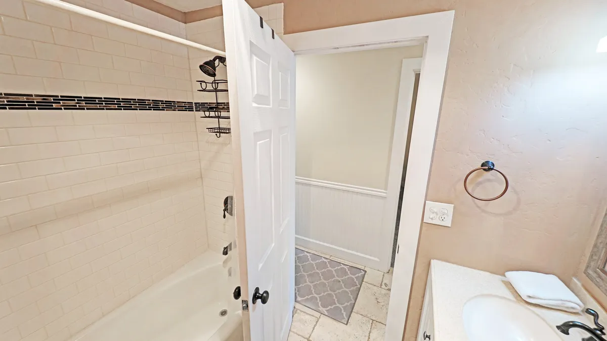 A modern and inviting bathroom featuring a bathtub, sink, towel rack, and a view through the open doorway. The space is clean, practical, and well-lit—ideal for freshening up after a day of adventure.